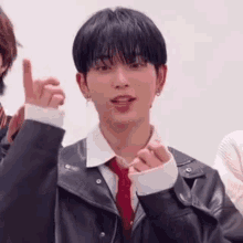 a young man wearing a leather jacket and tie is making a heart with his hands .