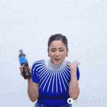 a woman in a blue sweater is holding a bottle of soda and making a funny face .