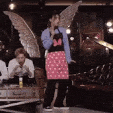 a woman wearing a minnie mouse apron and wings is standing in front of a group of people .