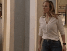 a woman in a white shirt and jeans is standing in a hallway .
