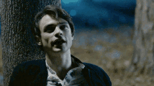 a man leaning against a tree at night with his mouth open