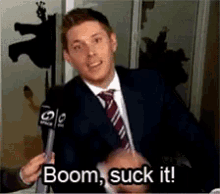 a man in a suit and tie is holding a microphone and says boom suck it .