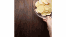 a person is holding a bowl of potatoes on a wooden table .