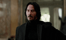 a man in a suit and turtleneck is standing in a hallway with his eyes closed