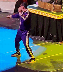a man in a purple tracksuit is standing on a blue surface