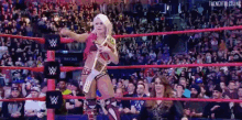 a woman is standing in a wrestling ring holding a wrestling belt .
