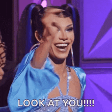 a drag queen is making a funny face and smiling while holding her hand to her forehead .
