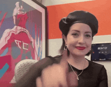 a woman wearing a black beret is giving the middle finger in front of a painting that says tc on it