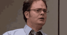 a man wearing glasses and a tie is sitting in an office .