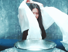 a woman with long black hair is standing in front of a glass bowl