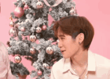 a man is standing in front of a christmas tree .