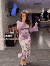 a woman in a purple and white floral dress is dancing in a hallway with a tiktok watermark