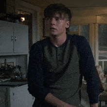 a young man in a green and blue shirt is standing in a kitchen