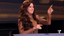 a woman with long hair is sitting at a table and giving a middle finger .