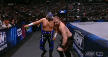 two wrestlers are standing next to each other on a wrestling ring in front of a crowd .