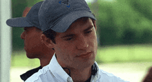 a man wearing a hat and a white shirt is standing next to another man .