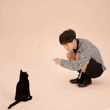 a man is kneeling down next to a black cat .