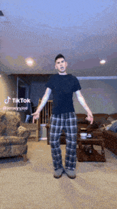 a man in plaid pajamas is standing in a living room with his arms outstretched in a tiktok video ..