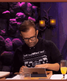 a man sitting at a table with a tablet and a glass of orange juice in front of him