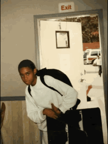 a boy with a backpack stands in front of an exit sign