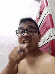 a shirtless man with glasses and a ring on his finger is laying on a bed