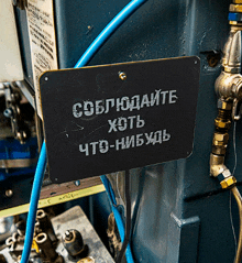 a black sign with russian writing on it hangs from a blue pipe
