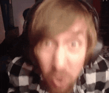 a man with a beard is wearing headphones and a plaid shirt .