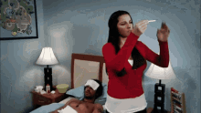 a woman in a red sweater is taking a picture of a man in a bed
