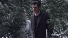 a man and a woman are walking in the snow with a hallmark drama logo in the background