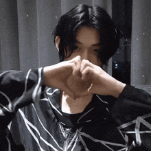 a man with long black hair is making a heart with his hands