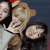 three girls are posing for a picture with one wearing a teddy bear costume .