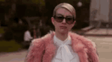a woman wearing sunglasses and a pink fur coat is walking down a street .