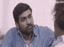 a man with a beard is talking to another man while wearing a blue shirt .