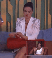 a woman in a white jacket is sitting on a couch with a red pillow .