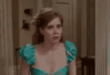 a woman in a blue dress is standing in a room looking at the camera .