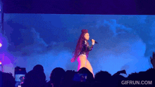 a woman is singing into a microphone in front of a crowd and the website gifrun.com is visible