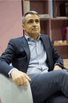 a man in a suit sits in front of a pink bookshelf