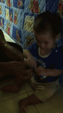 a child is playing with a cell phone on the floor in front of a quilt with teddy bears on it