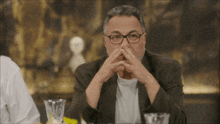 a man with glasses is sitting at a table with his hands on his face
