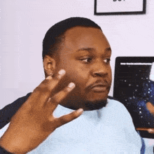 a man in a blue shirt is making a funny face while sitting in front of a computer monitor .