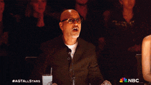 a man covering his mouth while sitting in front of a crowd with a nbc logo behind him