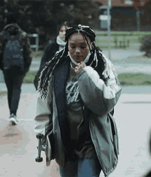 a woman wearing a mask and a jacket is walking down the street with a skateboard .
