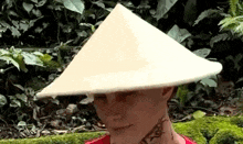 a man wearing a conical hat with a tattoo on his neck is standing in the woods .