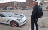 a man is standing in front of a white sports car with a toronto content fund banner above his head