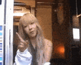 a woman with blonde hair is pointing at the camera while standing in a room .