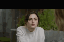 a woman in a white sweater is sitting on a couch looking at the camera .