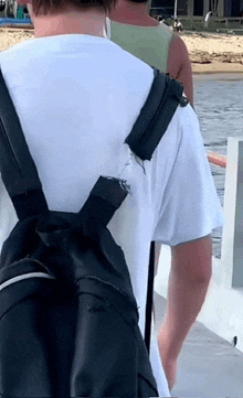 a man wearing a white t-shirt and a black backpack is walking on a boat .