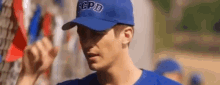 a man wearing a blue hat and a blue shirt is standing in front of a crowd of people .