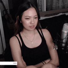 a woman in a black tank top sits in front of a microphone with a $ 500 sticker on her arm