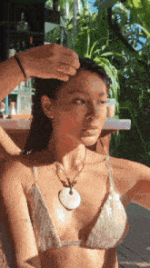 a woman in a bikini with a necklace on her neck looks at the camera